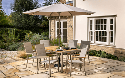 Image of Hartman Ezra 6 seater garden furniture dining set with parasol, situated on a patio next to a house