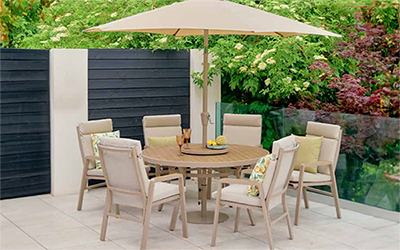 LG Sorrento 6 seat dining set, with cream metal chairs and wooden style slatted table top, parasol and lazy susan, on a patio in a garden