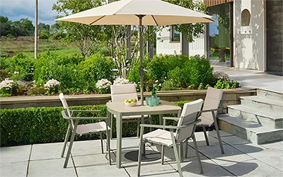 LG Tuscany 4 seat dining set, with padded seats, green metal frame and parasol, on a patio in a garden 