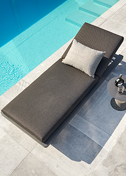 Metal framed sun lounger with grey cushion and pattern scatter cushion, on a stone patio with open door in background