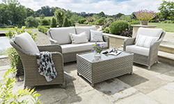 Kettler Cora wooden furniture with a rope wrap on teh back and arms. You find a 3seat sofa, 2 seat sofa , 2 lounge chairs and a low coffe table all sittign on a rug in a spacious conservatory (though it's suitable for external use). It is beautifully decorated for with cushions, blankets, drinkware and potted plants - with more distributed around the conservatory. With comfortable cushions and nice design it will look great and sit you comfortably in any space.