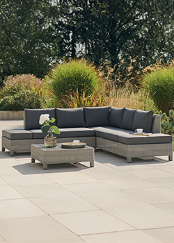 Grey garden furniture corner set with cushions on a metal frame, and wooden topped square coffee table. Trees in background.