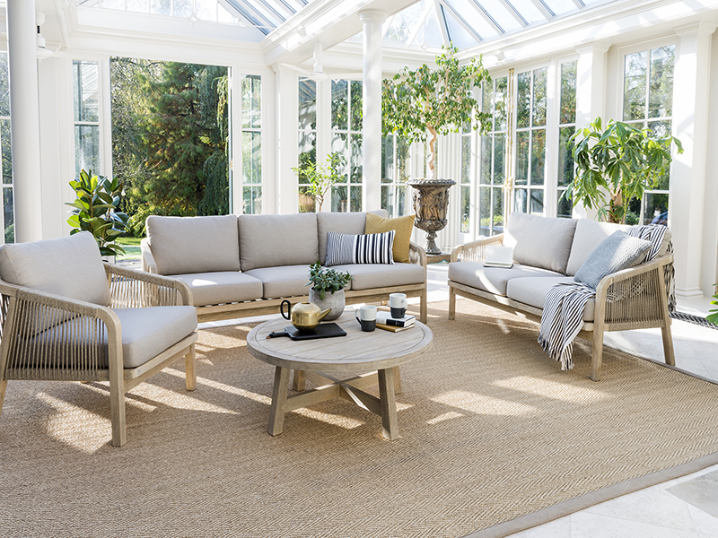 Kettler Cora rope garden furniture set. A 3 seat sofa, 2 seat sofa, single lounge chair and table; all positioned on a rug in a conservatory. The items are all beautifully decorated with cushions or drinkware and potted plants